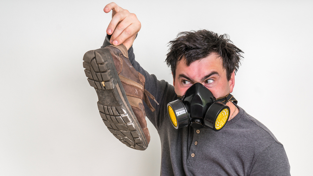 Mann mit Gasmaske hält schmutzigen, stinkenden Arbeitsschuh hoch